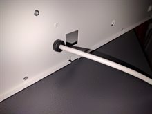 Närbild på vit metallpanel med svart kabelgenomföring och vit kabel, sett snett uppifrån.