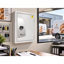 Ljusgrått väggmonterat säkerhetsskåp med digitalt kodlås och handtag, dörren stängd, i kontorsmiljö.